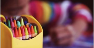 pack of crayons in the foreground with child coloring in the background